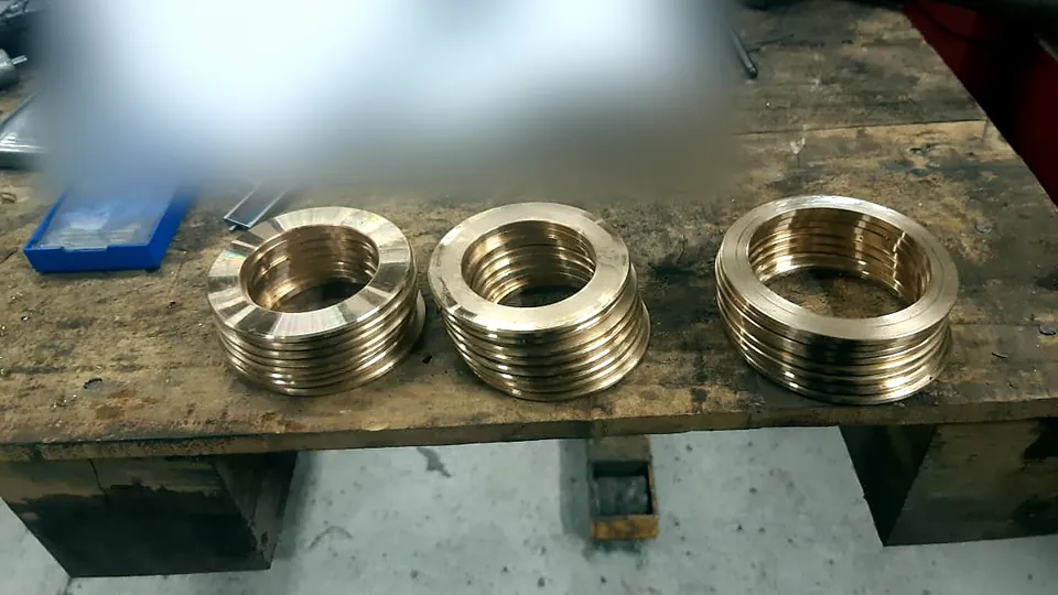 Tres pilas de anillos de bronce torneados sobre banco de madera del taller