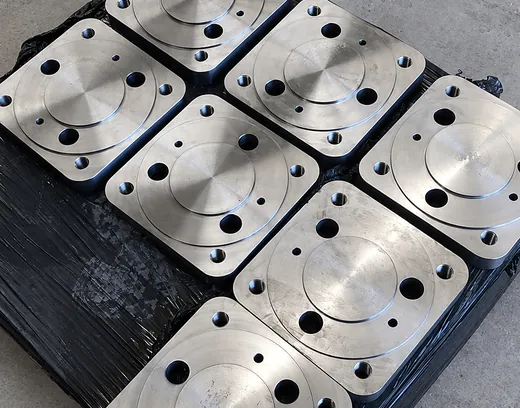 Ocho placas de acero mecanizadas con rebaje circular y perforaciones sobre pallet