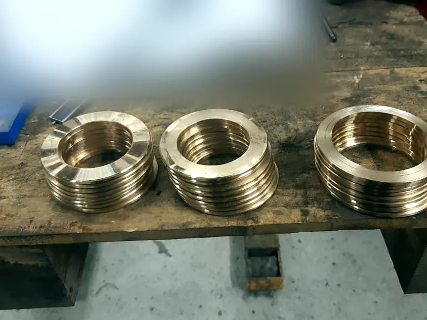 Tres pilas de anillos de bronce torneados sobre banco de madera del taller