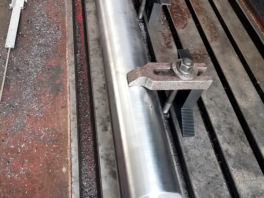 Barra de acero mecanizada sujeta con bridas sobre mesa ranurada de fresadora en taller