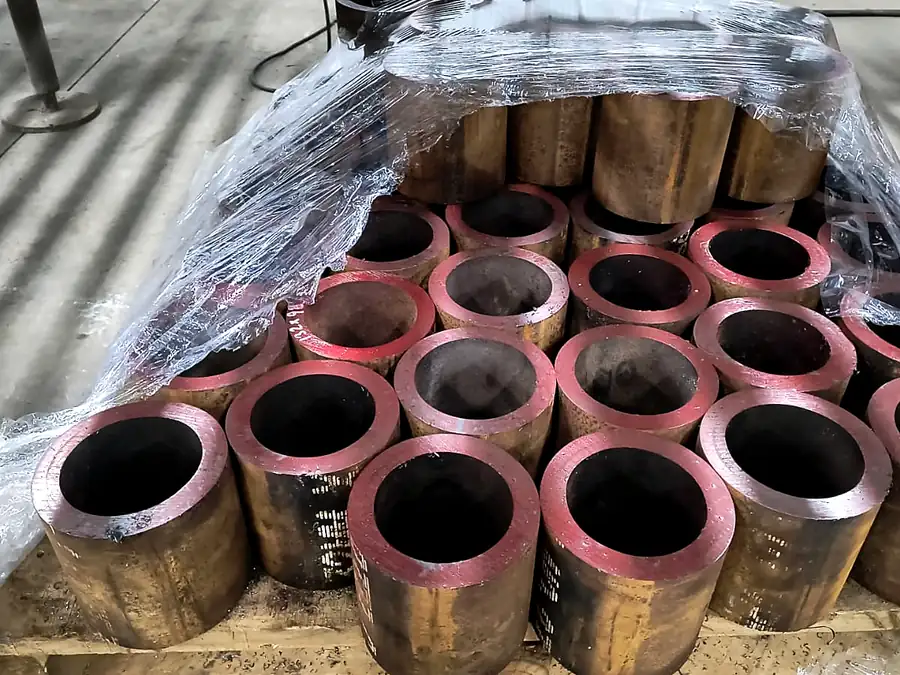 Tramos de barra hueca de bronce con caras pintadas de rojo apilados en pallet