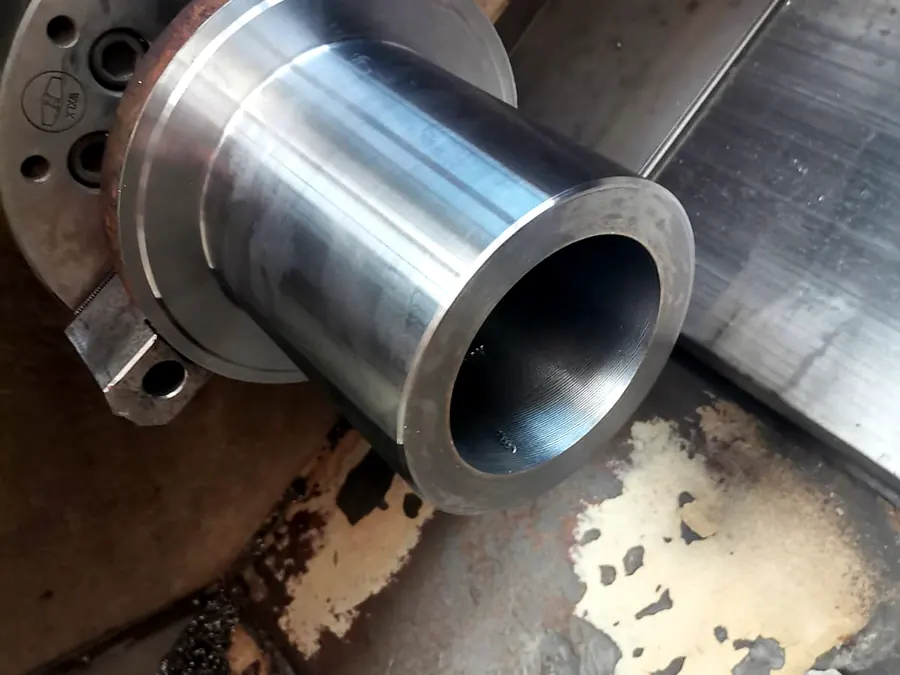 Pieza tubular de acero con pestaña recién torneada sujeta en el plato del torno