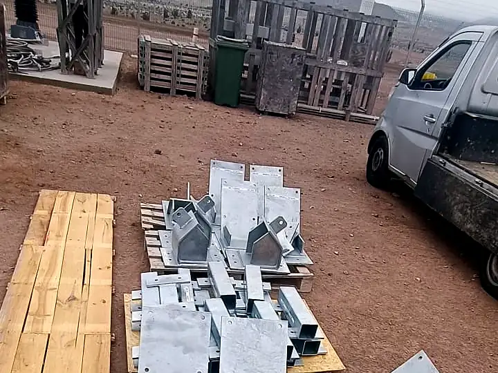 Soportes galvanizados sobre pallets en un patio de tierra junto a una camioneta