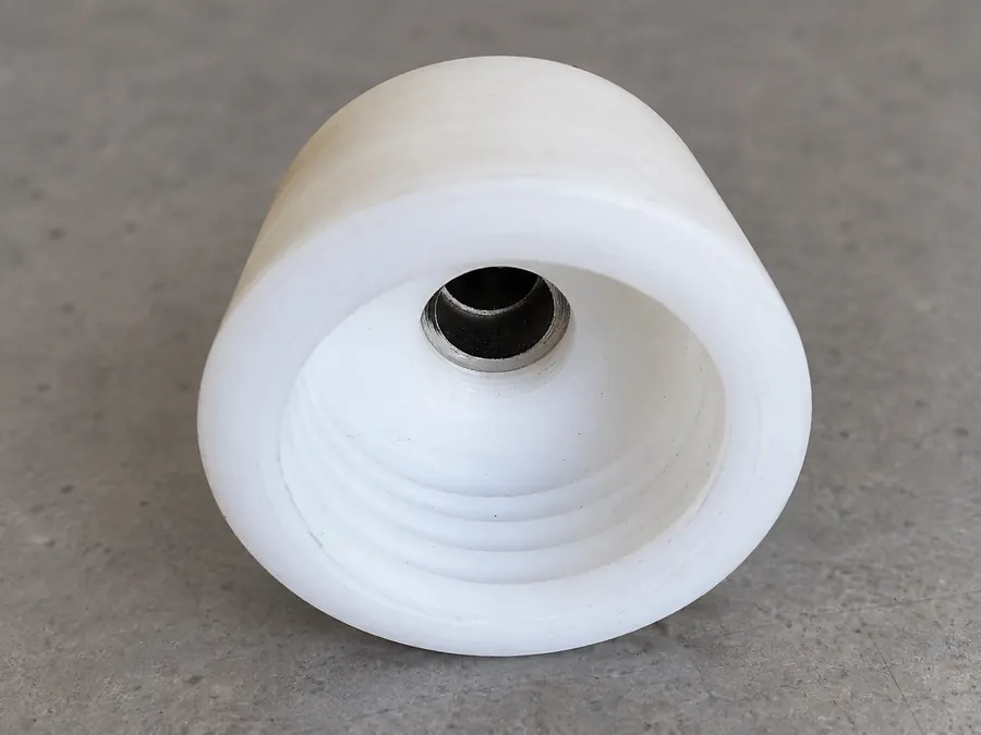 Pieza cilíndrica de plástico blanco torneada con interior escalonado e inserto metálico