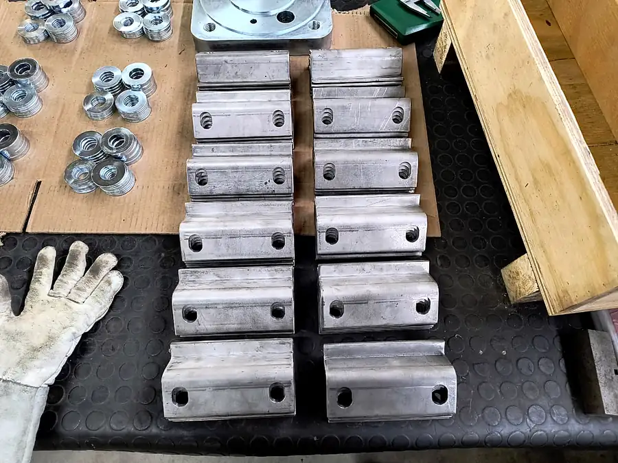 Serie de piezas de acero perfiladas con dos agujeros ordenadas en mesa de taller