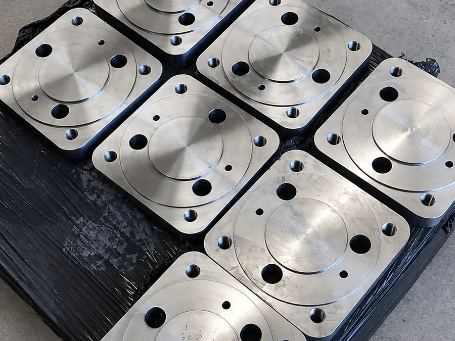 Ocho placas de acero mecanizadas con rebaje circular y perforaciones sobre pallet
