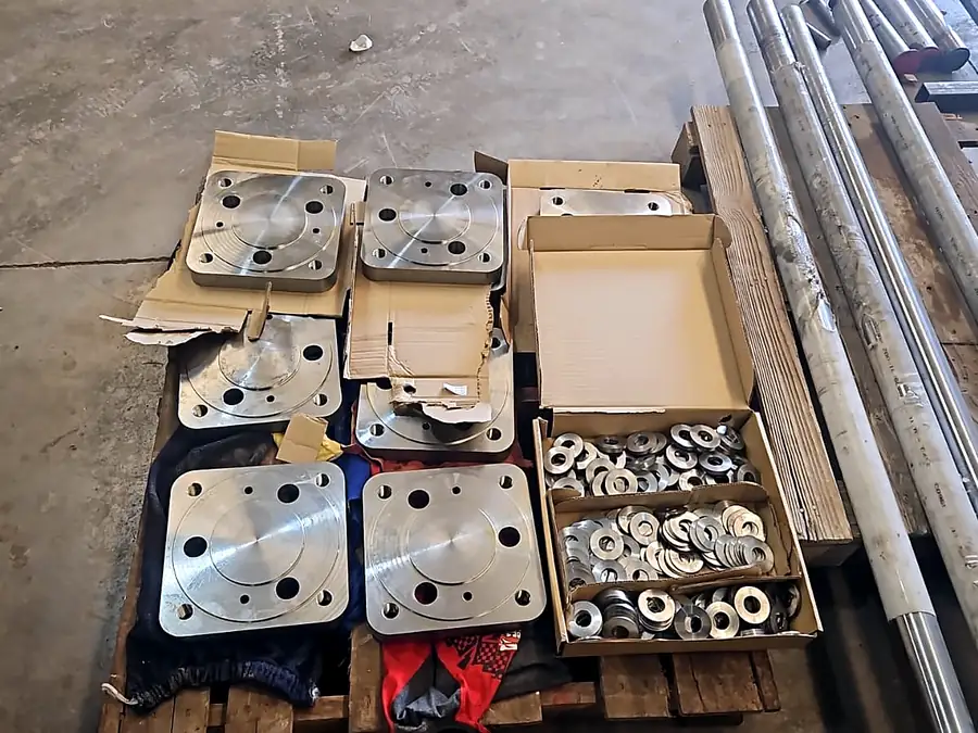 Placas cuadradas mecanizadas en cajas de cartón junto a golillas y barras redondas