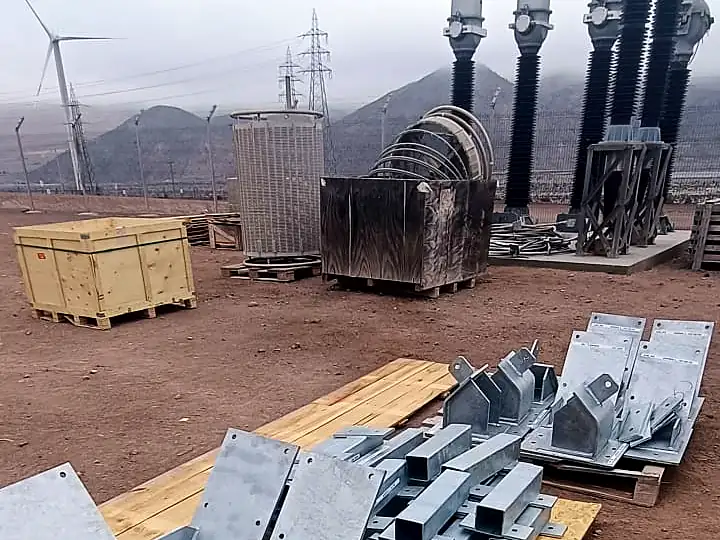 Piezas de acero galvanizado en faena de subestación eléctrica con aerogenerador al fondo