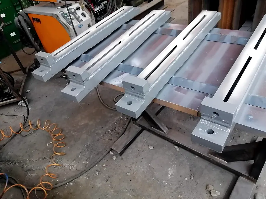 Soportes de acero ranurados con soldadura visible y pintura gris en el taller