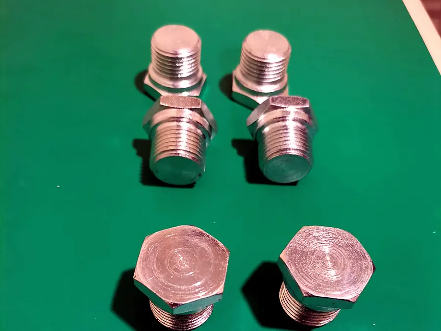 Seis tapones hexagonales roscados de acabado brillante sobre superficie verde